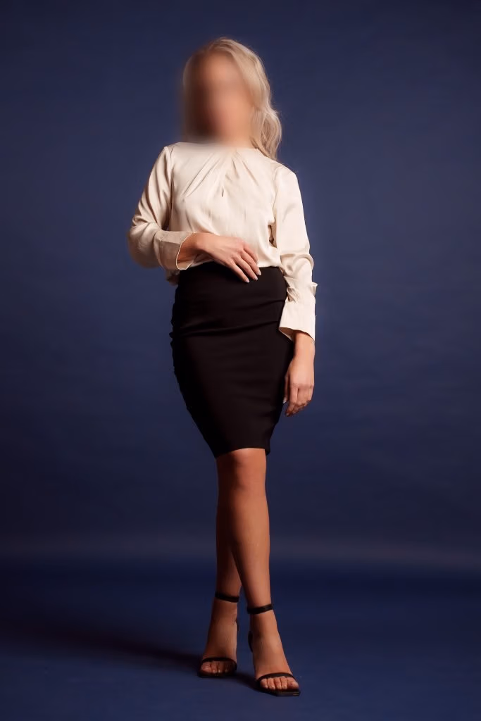 Woman wearing a cream blouse and black pencil skirt, standing with one hand on her hip.